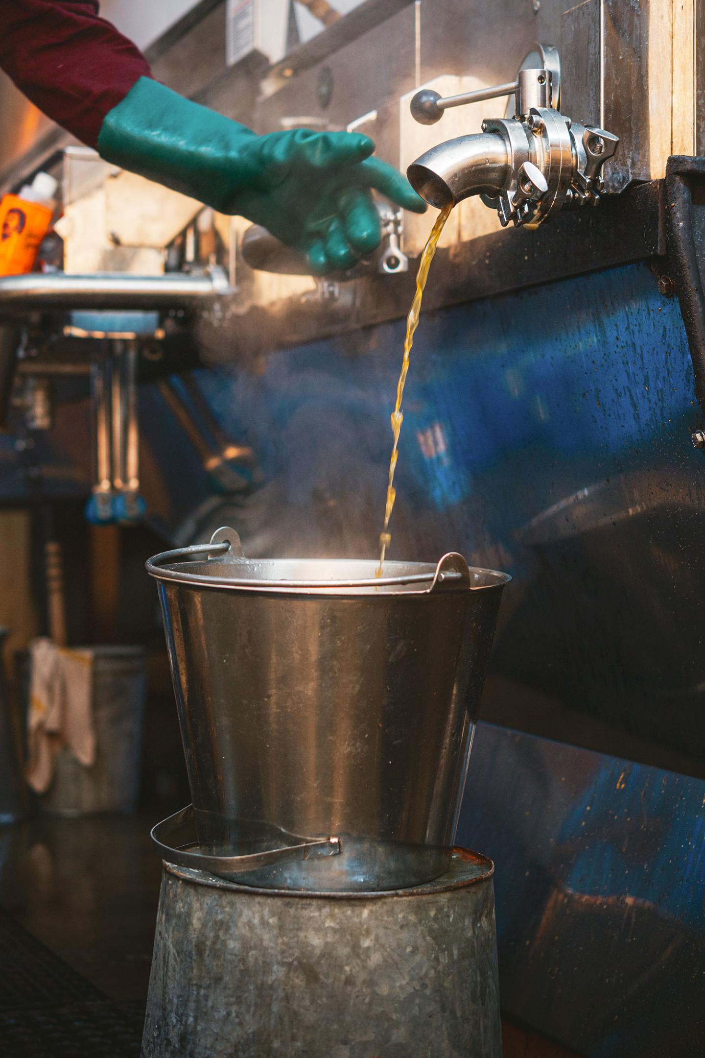 Hot liquid pouring into a steaming metal bucket from a spout.