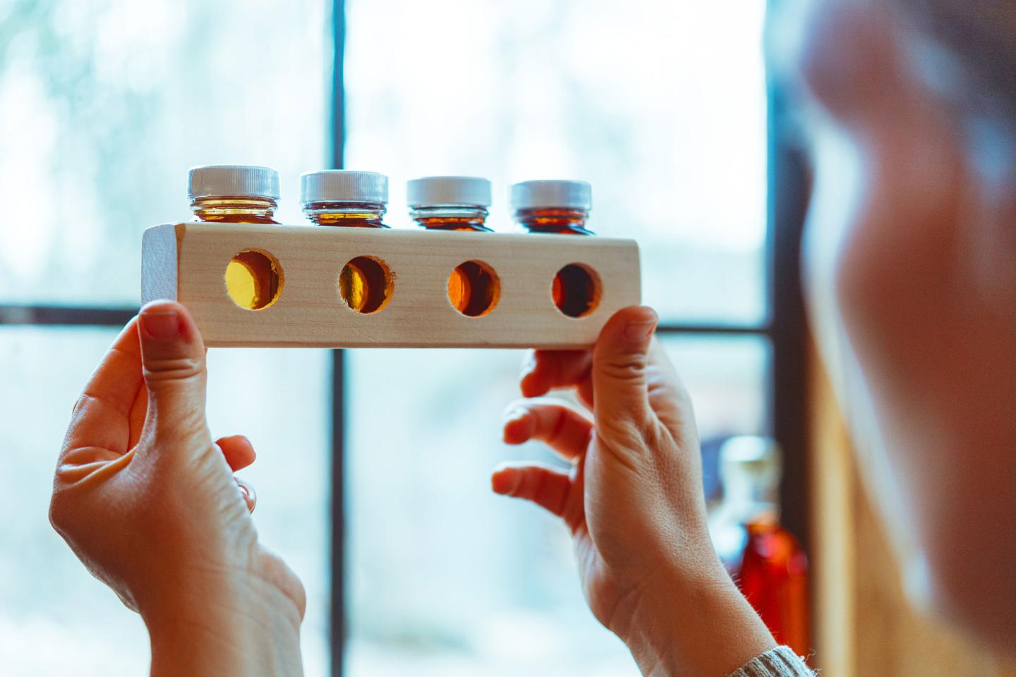 Hands holding a wooden stand with four small jars of amber liquid.